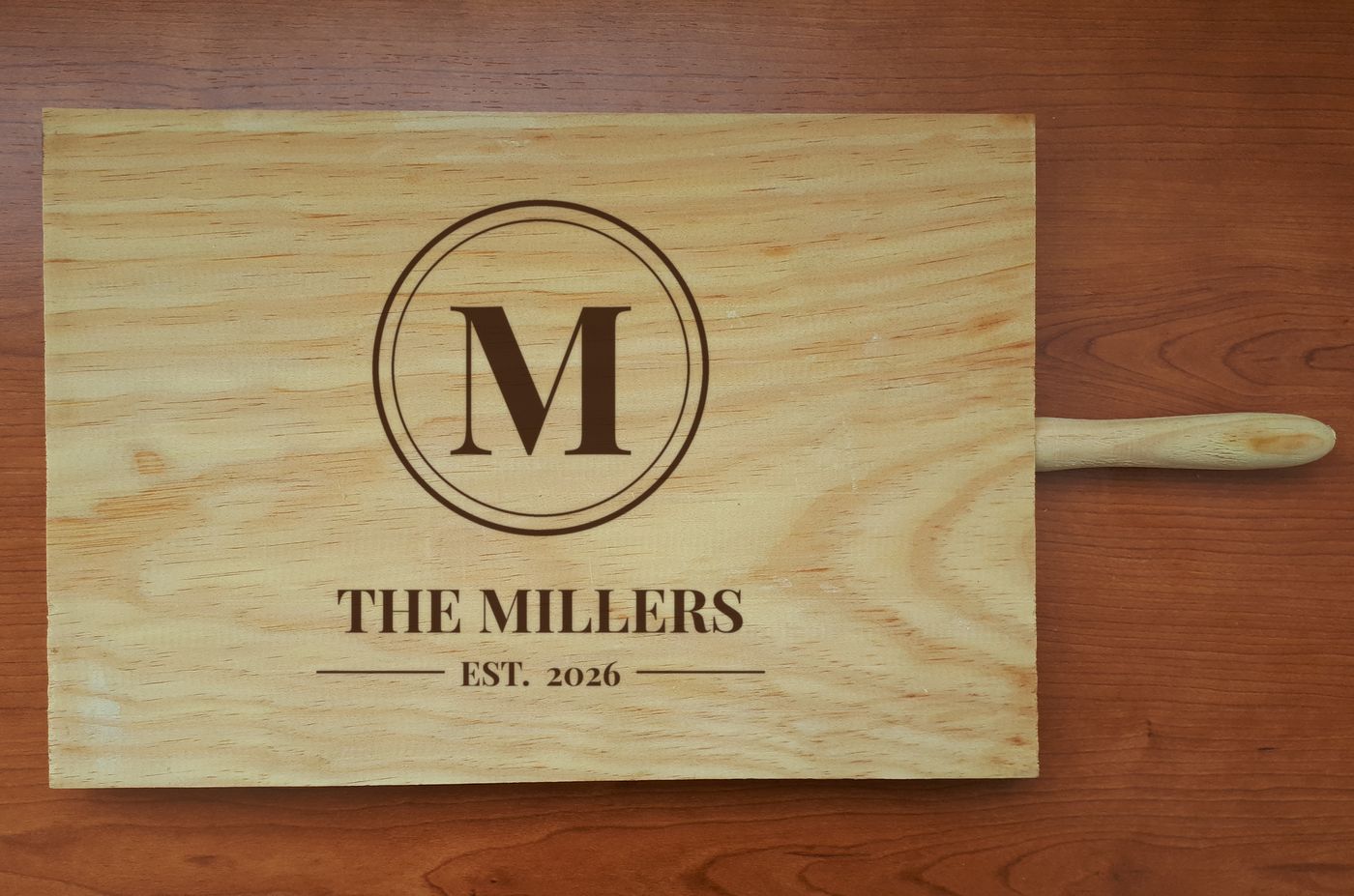 Wood cutting board engraved with a monogram M, the words The Millers, and Est. 2026.